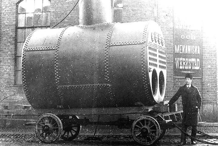 A big steam engine outside JMW. A man in a suit and hat is standing next to it. The photo is black and white.