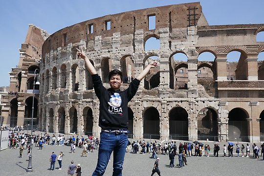 Man reaching his arms up in the air in front of the Colosseum 