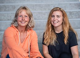 Charlotta Mellander sits to the left and Orsa Kekezi sits to the right. Both are sitting on the steps in JIBS' entrance hall. 